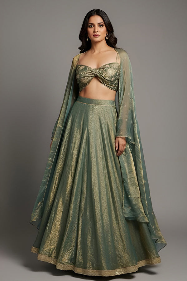 Woman wearing a green traditional outfit with a matching dupatta on a gray background